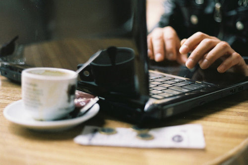 Девушка без маникюра работает дома на ноутбуке черного цвета с чашечкой кофе