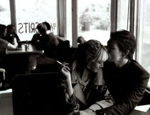 Парень целует курящую женщину в висок в кафе за столиком