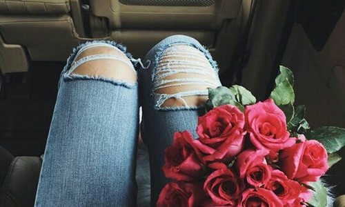 девушка с букетом красных роз в джинсах с порваными коленками в машине