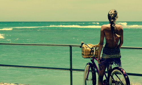 девушка на велосипеде со спины любуется морскими волнами