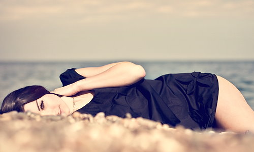 девушка в черном мокром платье лежит на берегу моря
