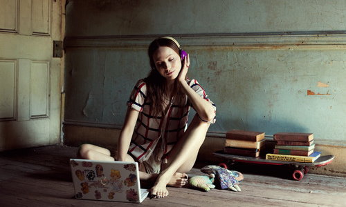 девушка наслаждается музыкой в наушниках слушая сидя на полу перед ноутбуком