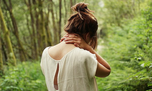 Девушка с гулькой со спины в лесу держит себя за шею сзади