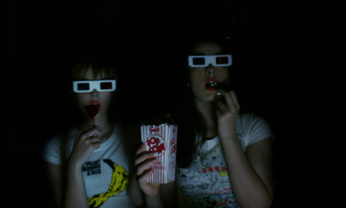 две девушки в 3d очках в кинотеатре кушают попкорн
