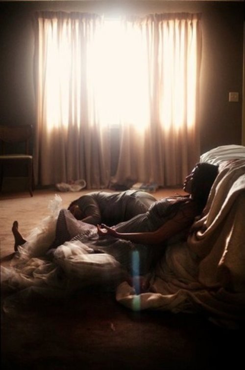 Девушка сидит на полу опершись на кровать, а рядом спит мужчина