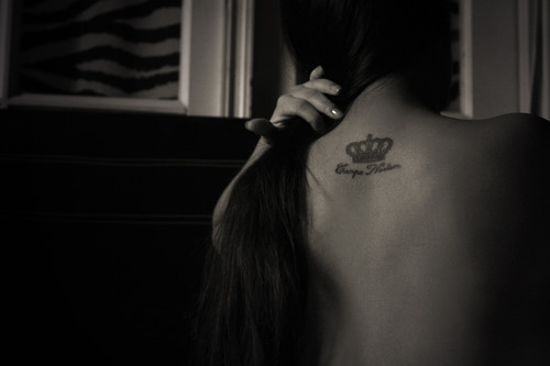 Девушка убрала волосы, чтоб показать на спине татуировку короны