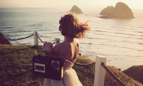 девушка прогуливается вдоль моря с магнитофоном на плече