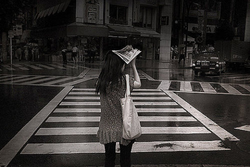 девушка прячется от дождя под газетой переходя улицу