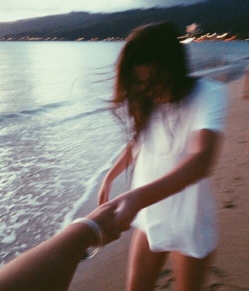 смазанное фото девушки которая держит своего парня за руку на берегу
