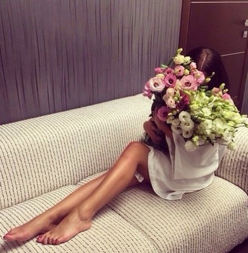 девушка прячет лицо за букетом цветов сидя на диване в халатике