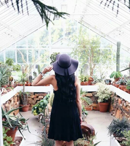 девушка в шляпе со спины в черном платье среди растений