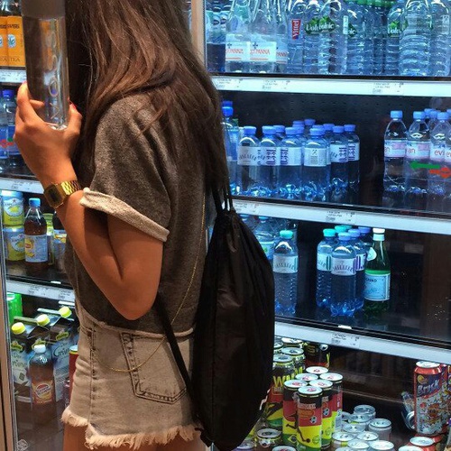 девушка в серой футболке без лица идет вдоль полок магазина с бутылкой