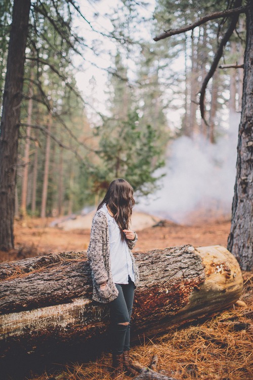 девушка в осеннем лесу на спиленном дереве без лица смотрит на дым от костра