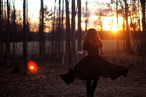 девушка в черном платье кружится в осеннем лесу на закате вдалеке