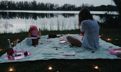 девушка со спины на берегу озера в ожидании романтического ужина при свечах