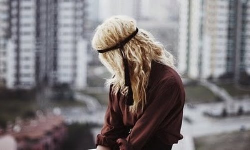 блондинка с повязкой в волосах без лица за спиной многоэтажки города