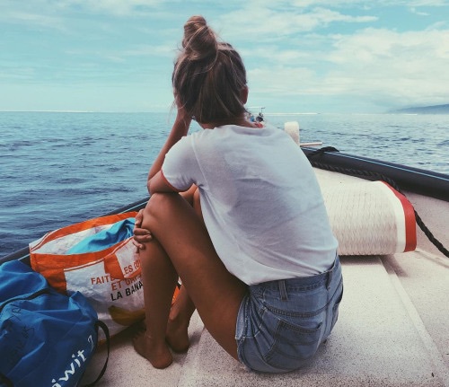 блондинка с пакетами со спины сидит смотрит вдаль без лица на лодке в море
