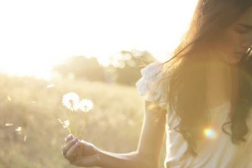 брюнетка в легком белом платье в поле с одуванчиками в лучах солнца