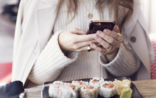 девушка фотографирует суши в свитере и пиджаком на плечах