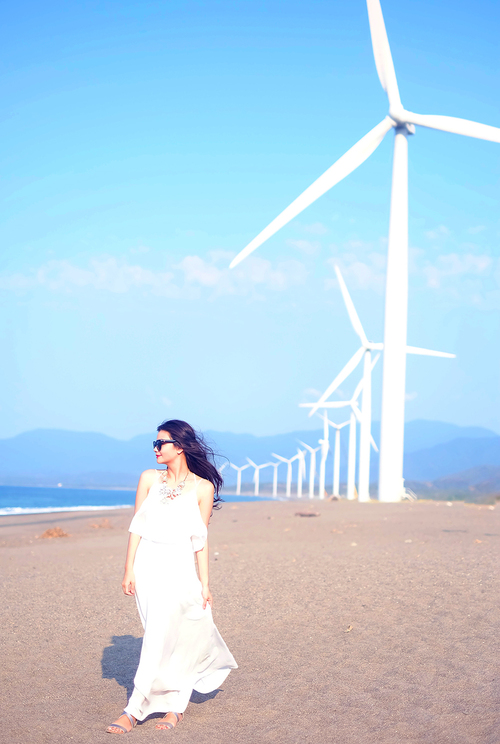 брюнетка в белом платье на берегу океана возле ветряных мельниц