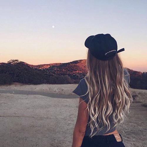 девушка с белыми кончиками волос спиной в кепке смотрит на полную луну в небе