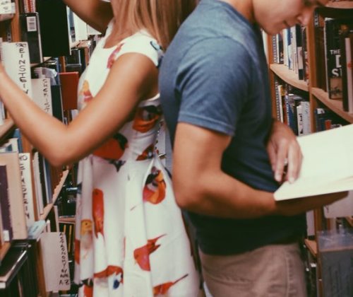 парень с девушкой в библиотеке прикасаются спинами