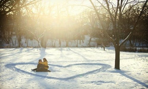 влюбленные сидят внутри сердца нарисованного на снегу в солнечный зимний день лав стори