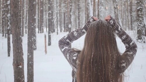 девушка в свитере с оленями со спины в лесу идет первый снег