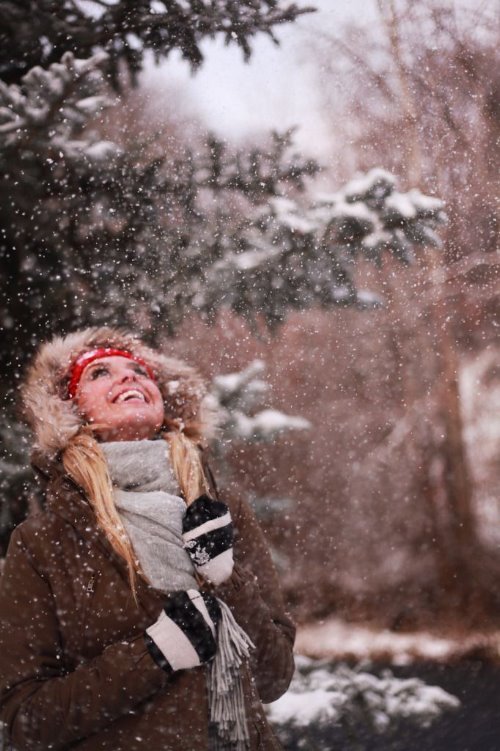 блондинка в капюшоне под елкой радуется первому снегу