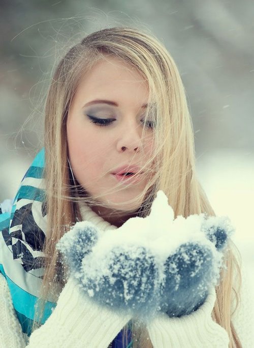 блондинка дует на снег в ладошках