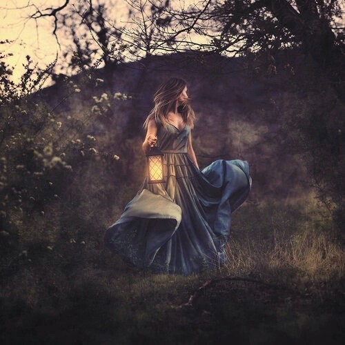 девушка в длинном синем платье бежит по лесу с фонарем