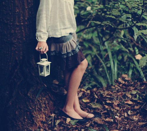 ноги девушки держащей фонарь в лесу возле дерева