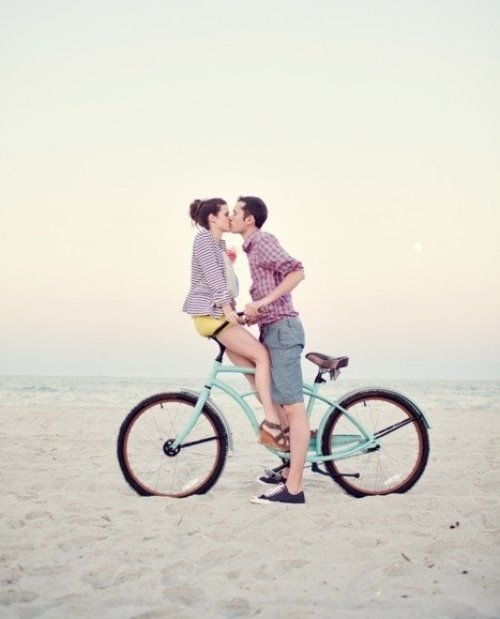 влюбленные целуются сидя на велосипеде на берегу океана