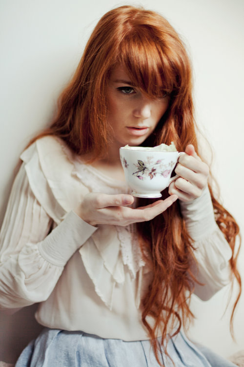 рыжая девушка с длинными волосами в белой блузке с кружкой чая