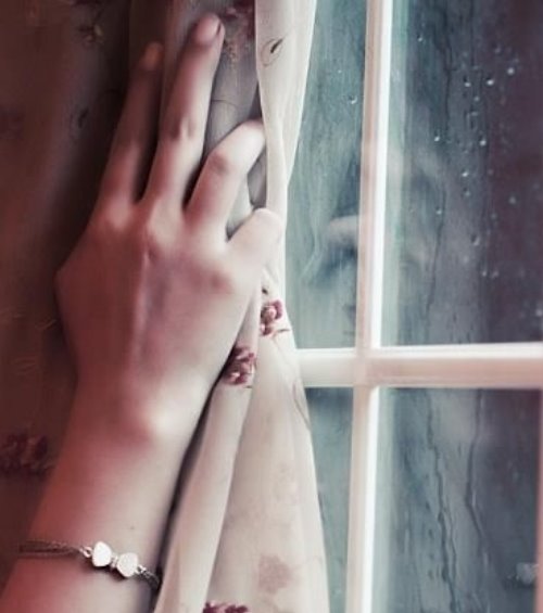 рука девушки на шторах возле окна с каплями дождя