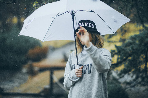 девушка в серой толстовке с кепкой под зонтом осенью