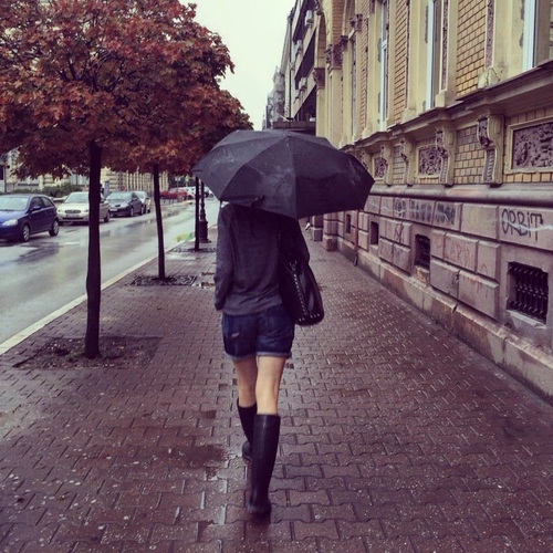 девушка в резиновых сапогах со спины шагает по городу под зонтом осенью