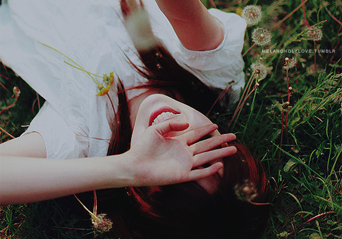 девушка лежит в траве с одуванчиками закрывая лицо