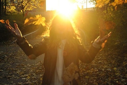 девушка подбрасывает осенние листья в лучах солнца