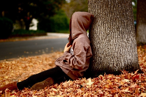 девушка в капюшоне сидит под деревом