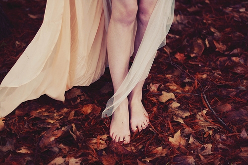 ноги девушки на рыжих осенних листьях в парке в длинном платье