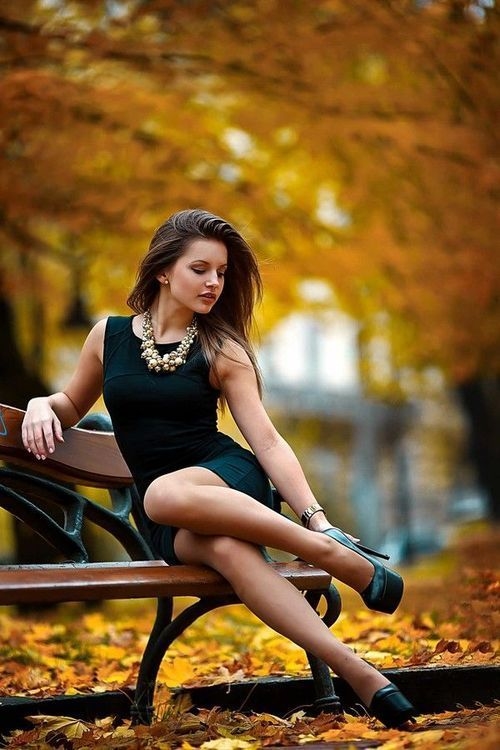 девушка в маленьком черном платье на скамейке в парке под золотыми деревьями осенью
