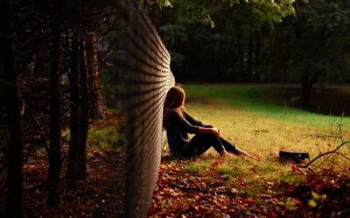 девушка сидит под забором на осенней поляне