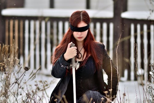 девушка с завязанными черной повязкой глазами держит меч, шпагу