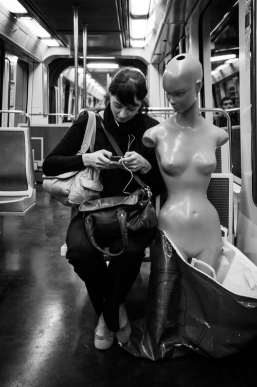 манекен в метро сидит рядом с девушкой с мобильным телефоном в руках