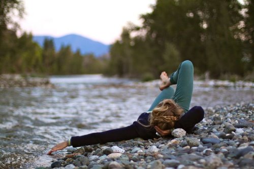 девушка лежит на спине на каменном берегу мокая руку в реку