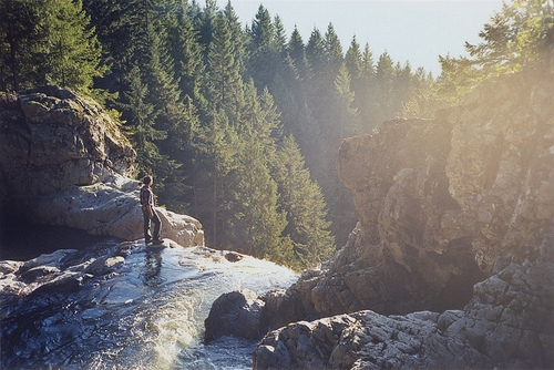 парень стоит на вершине водопада среди каменных гор
