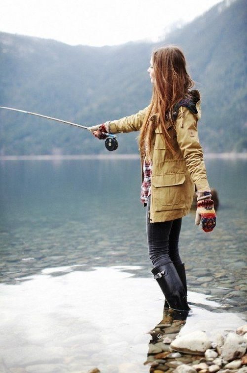 девушка ловит рыбу стоя на камнях в резиновых сапогах осенью