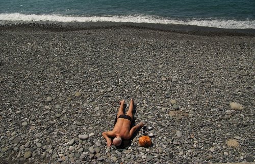 мужчина загорает на галечном пляже лежа на животе