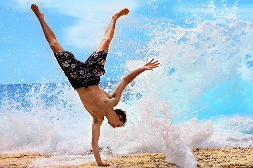 парень стоит на одной руке в морских волнах летом в плавках